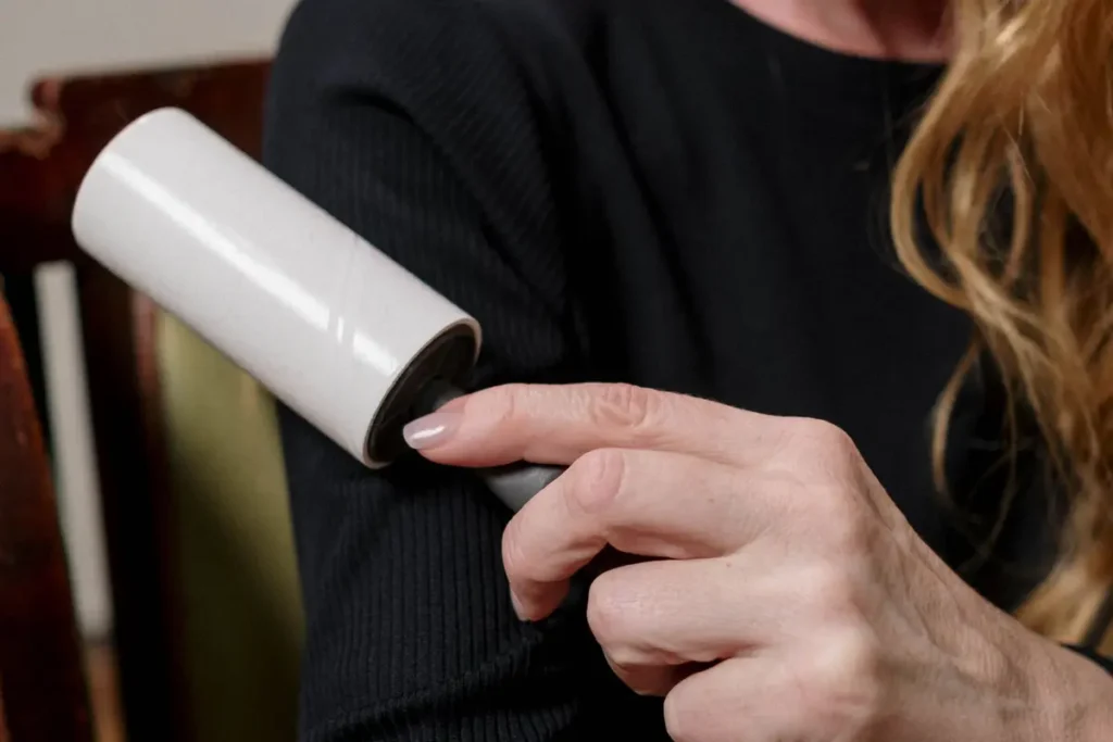 Person using a lint roller on the sleeve of a black sweater